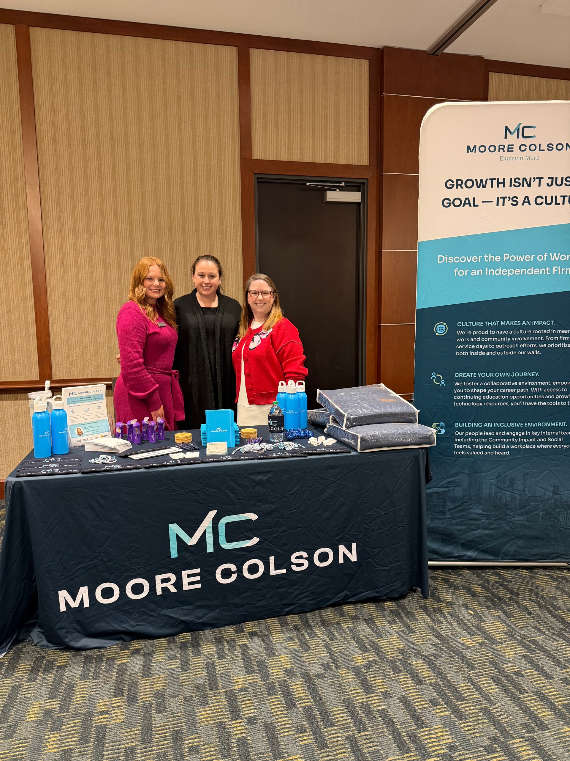 Moore Colson employees standing behind a branded booth at an on-campus visit.