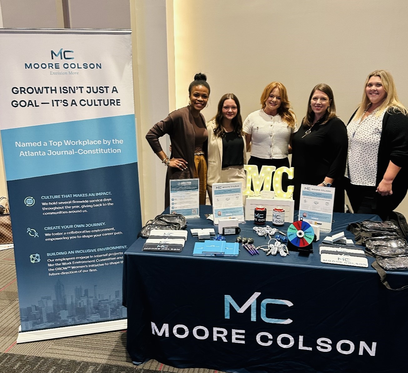Moore Colson employees standing behind a branded booth at an on-campus recruiting event.