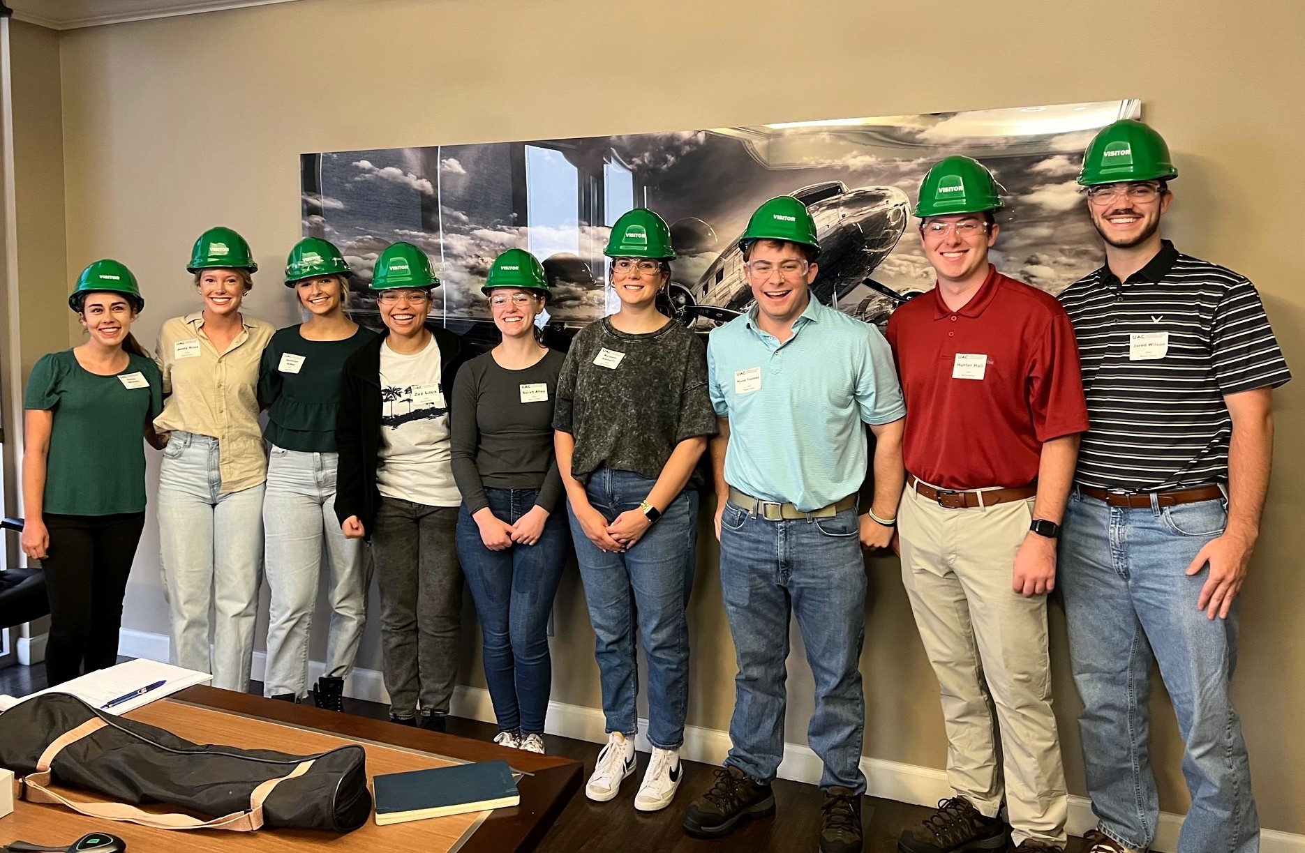A group of Moore Colson interns wearing hardhats, standing and smiling at an on-site client event.