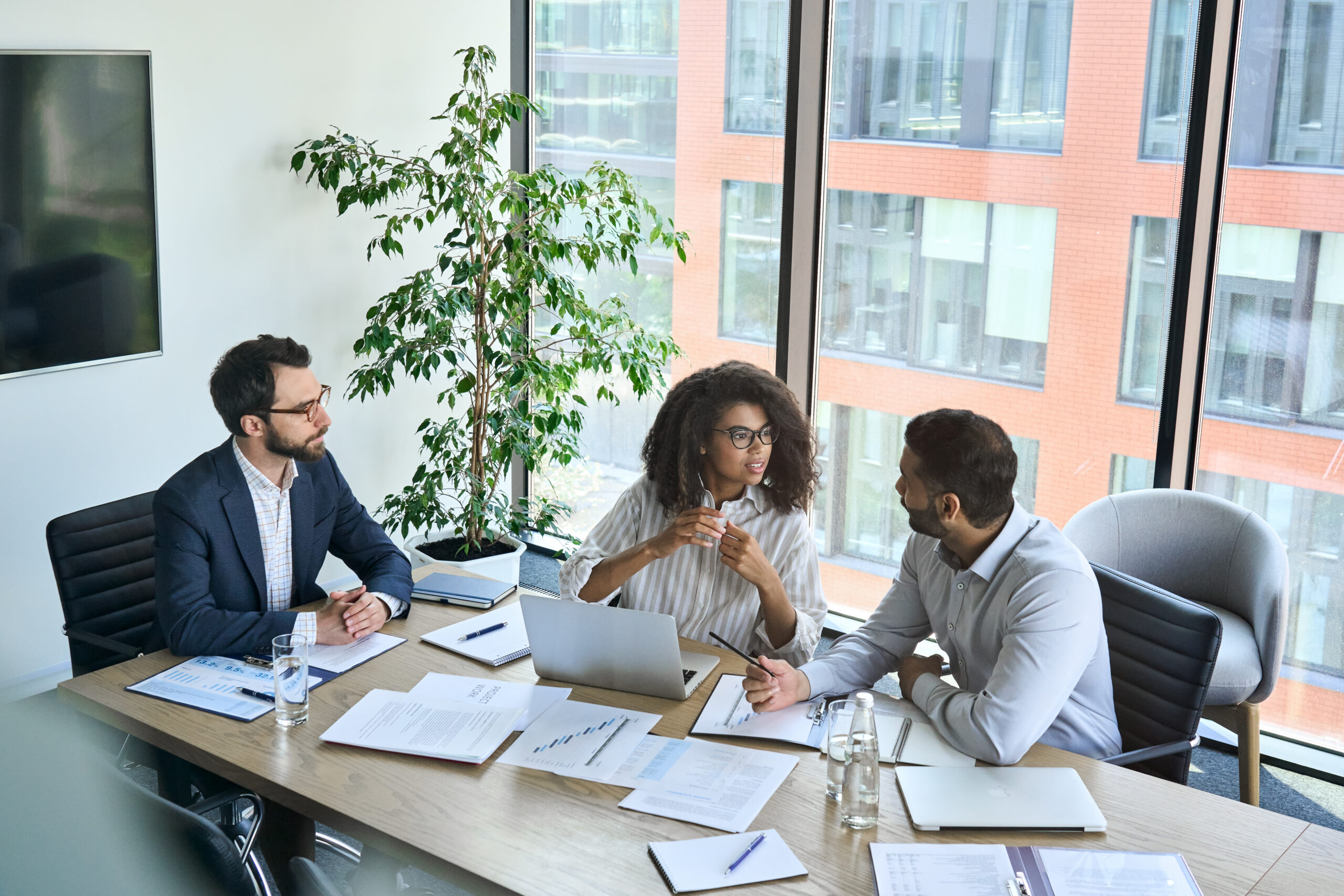 Three professionals at a conference table reviewing documents during a buy-side M&A advisory meeting