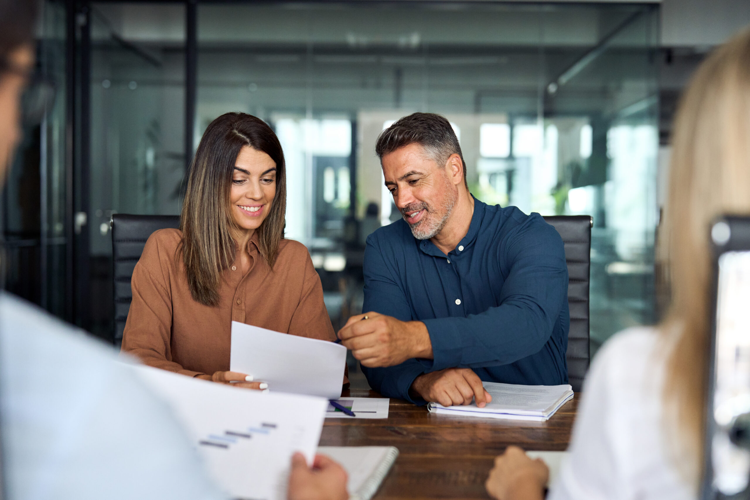 Professionals in a midsize business working on corporate tax documents in an office. Smiling business executives and corporate tax CPAs having discussion on business tax strategy sitting at board room table.